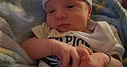 Dallas is registered to the contest to win money with this photo: newborn, baby, infant, child, portrait, striped_cap, onesie, blanket, swaddled, lying_down, face, hands, eyes_open, indoor, nursery, crib, cozy, text_on_clothing, family, photograph