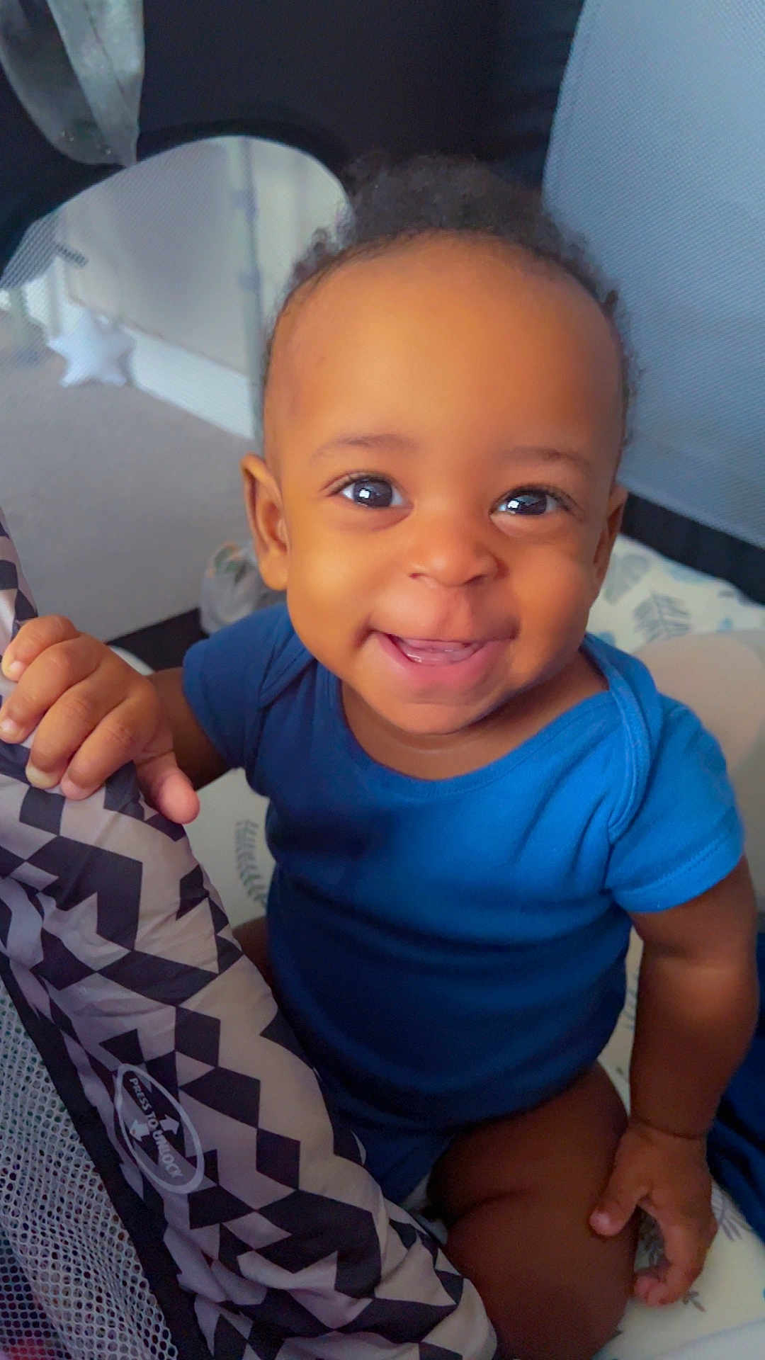 Carl joined the competition — help win amazing prizes! baby, child, smiling, blue_onesie, indoor, playpen, hand, face, cute, happy, infant, person, skin, young_child, eyes, mouth, fingertips, pattern, fabric, seated
