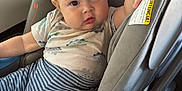 Austhin is registered to the contest to win money with this photo: baby, car_seat, child, infant, dinosaur_print, striped_pants, clothing, seatbelt, car_interior, hand, face, eyes, cute, comfort, sitting, child_safety, transportation, person, young_child, curious