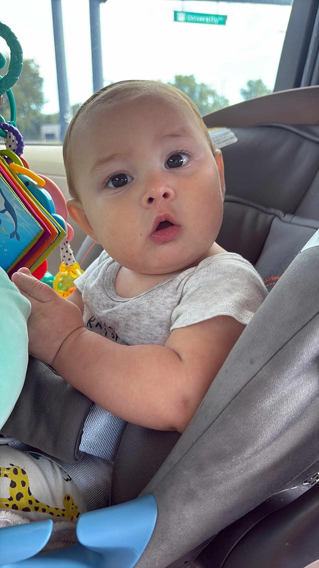 Austhin joined the competition — help win amazing prizes! baby, child, car_seat, toy, colorful, curious, face, wide_eyes, open_mouth, clothing, seatbelt, window, car_interior, soft_light, closeup, infant, person, cute, indoor, portrait