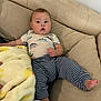 baby, child, couch, blanket, striped_pants, dinosaur_shirt, foot, hand, face, curious, indoors, living_room, soft_texture, sitting, relaxed, casual_clothing, infant, comfort, home, expression