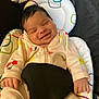 baby, smiling, onesie, infant, cushion, baby_seat, patterned, cherry_pattern, flower_pattern, happy, closeup, face, hand, sleepy, cute, child, indoor, comfort, soft, resting