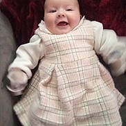 Lila joined the competition — help win amazing prizes! baby, infant, smiling, plaid_dress, white_sleeves, blanket, indoor, soft_fabric, happy, child, portrait, cute, warm, furniture, cozy, sitting, young_child, apparel, patterned_clothing, human