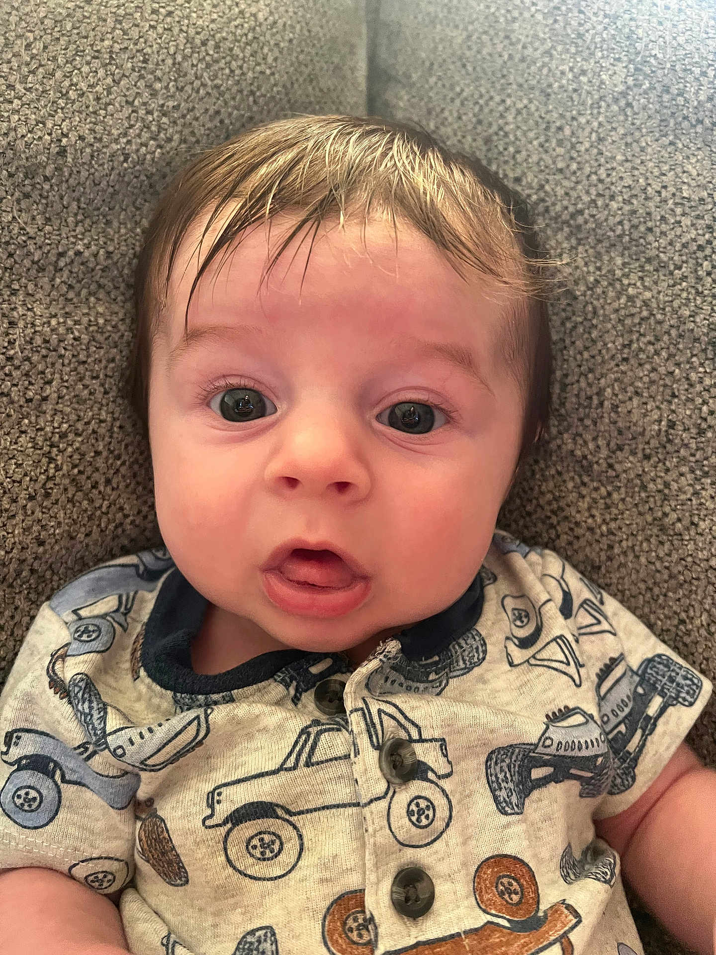 Hayden joined the competition — help win amazing prizes! baby, child, face, eyes, mouth, shirt, clothing, pattern, vehicle_print, couch, fabric, texture, indoor, portrait, infant, expression, sitting, cute, young, person