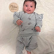 Celeste joined the competition — help win amazing prizes! baby, infant, three_months, milestone_disc, wooden_sign, blanket, onesie, floral_print, bow, earring, smiling, portrait, indoors, lying_down, soft_texture, cozy, newborn, adorable, dark_hair, baby_clothes