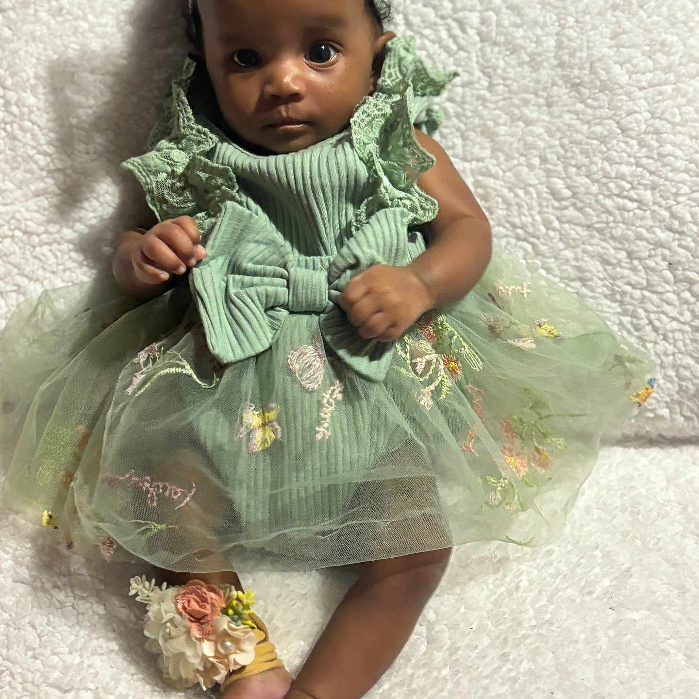 Yanni joined the competition — help win amazing prizes! accessory, anklet, baby, barefoot, blanket, child, clothing, curly_hair, cute, floral_embroidery, footwear, green_dress, headband, indoor, infant, person, portrait, sitting, textured_blanket, young_child