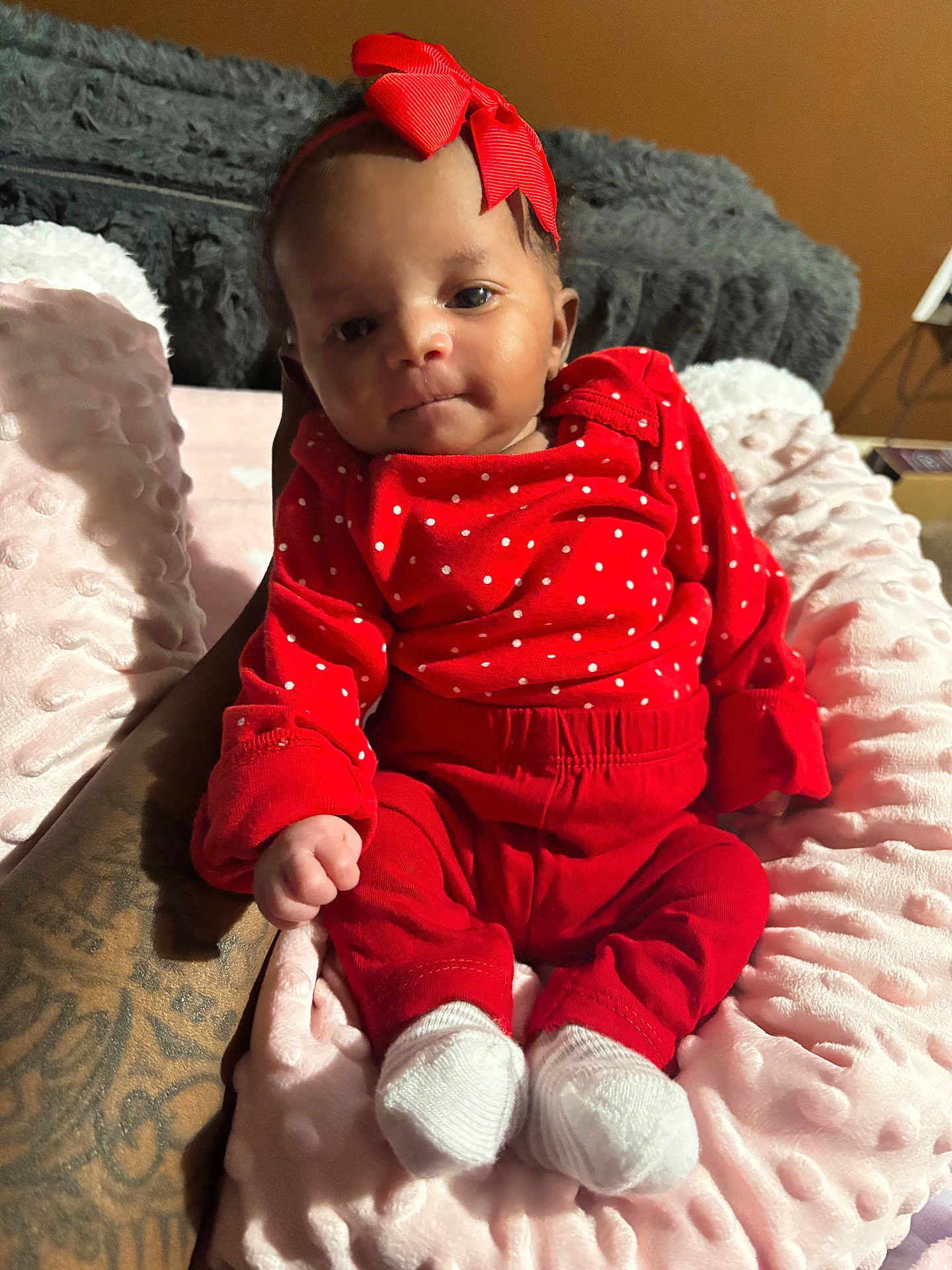 Yanni joined the competition — help win amazing prizes! baby, infant, red_clothing, polka_dots, headband, bow, tattoo, hand, blanket, soft_texture, white_socks, cute, indoor, portrait, person, newborn, resting, cozy, child, human
