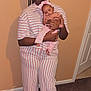 Yanni is registered to the contest to win money with this photo: child, baby, indoor, striped_clothing, pink, white, pajamas, holding, headband, bow, carpet, door, calendar, wall, smiling, playful, portrait, person, footwear, family
