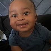 Micah joined the competition — help win amazing prizes! baby, smiling, child, face, portrait, blue_clothing, happy, cute, indoors, seated, head, skin, person, infant, young_child, expression, hands, background, textile, quilting