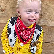 Brody joined the competition — help win amazing prizes! child, boy, costume, cowboy, yellow_shirt, red_bandana, sheriff_badge, blond_hair, spiky_hair, wood_background, portrait, smiling, standing, indoor, cute, fashion, young_child, person, fun, happy