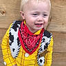 child, boy, costume, cowboy, yellow_shirt, red_bandana, sheriff_badge, blond_hair, spiky_hair, wood_background, portrait, smiling, standing, indoor, cute, fashion, young_child, person, fun, happy
