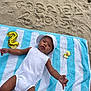 Gabriel participe au concours pour gagner de l'argent avec cette photo : baby, child, beach, sand, towel, striped_towel, white_clothing, hat, balloon, number_two, infant, lying_down, sunny, outdoor, celebration, cute, summer, skin, expression, relaxation
