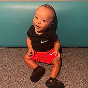 Gabriel a rejoint le concours — aidez-le/la à gagner de superbes lots ! baby, child, infant, sitting, nike, red_shorts, black_shirt, black_shoes, carpet, cushion, indoor, smiling, happy, cute, portrait, young_child, feet, clothing, person, head