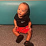 baby, child, infant, sitting, nike, red_shorts, black_shirt, black_shoes, carpet, cushion, indoor, smiling, happy, cute, portrait, young_child, feet, clothing, person, head
