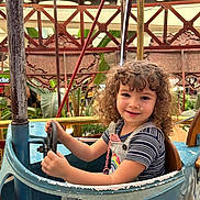Djodie a rejoint le concours — aidez-le/la à gagner de superbes lots ! child, curly_hair, smile, amusement_ride, steering_wheel, vintage, blue_car, outdoor, daylight, metal, rust, plants, greenery, carnival, playful, happy, person, seat, striped_shirt, overalls