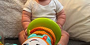 Freddie joined the competition — help win amazing prizes! baby, blanket, bright_colors, carpet, child, colorful, crib, cute, expression, floor, home, indoors, infant, person, pillow, playful, sitting, soft_texture, toy, white_clothing