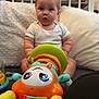 Freddie joined the competition — help win amazing prizes! baby, child, toy, colorful, carpet, pillow, blanket, crib, indoors, cute, sitting, playful, person, infant, white_clothing, soft_texture, bright_colors, expression, floor, home