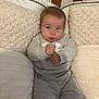 baby, child, infant, sitting, grey_clothing, sweatshirt, pants, cushion, pillow, crib, wooden_furniture, indoor, cute, expression, face, hands, cozy, soft_texture, neutral_colors, portrait