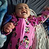 baby, infant, smiling, pink_clothing, minnie_mouse, onesie, blanket, bed, happy, cute, face, person, child, sleepwear, soft, lying_down, cozy, indoor, expression, cheerful