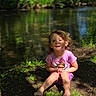 Brylee joined the competition — help win amazing prizes! child, smiling, outdoor, nature, river, greenery, sunlight, grass, sandals, curly_hair, pink_shirt, sitting, happy, forest_floor, daylight, young_child, casual_clothing, trees, water, relaxation