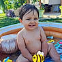 toddler, child, pool, water, summer, outdoor, inflatable_pool, toy, smiling, happy, grass, garden, sunlight, house, playing, wet_hair, sitting, cute, baby, fun