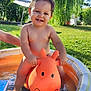 Sacha a rejoint le concours — aidez-le/la à gagner de superbes lots ! bare_chest, child, daylight, garden, giraffe_toy, grass, greenery, happy, inflatable_pool, orange_toy, outdoor, person, playtime, smiling, summer, sunny, toddler, toy, trees, water