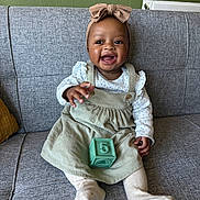 Charis joined the competition — help win amazing prizes! baby, child, smiling, sitting, couch, gray_couch, green_dress, headband, bow, toy_block, number_5, happy, indoor, person, long_sleeve, tights, radiator, wall, furniture, cute