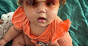 Halo is registered to the contest to win money with this photo: baby, child, sunglasses, orange_clothing, curly_hair, sitting, blanket, cute, indoor, skin, face, hand, foot, expression, fashion, accessory, toddler, infant, portrait, casual
