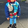 Sean joined the competition — help win amazing prizes! blue_pants, boy, casual_clothing, child, daytime, glasses, happy, jacket, outdoor, pavement, person, road, shadow, smiling, sneakers, standing, sunlight, thomas_the_tank_engine, urban, young