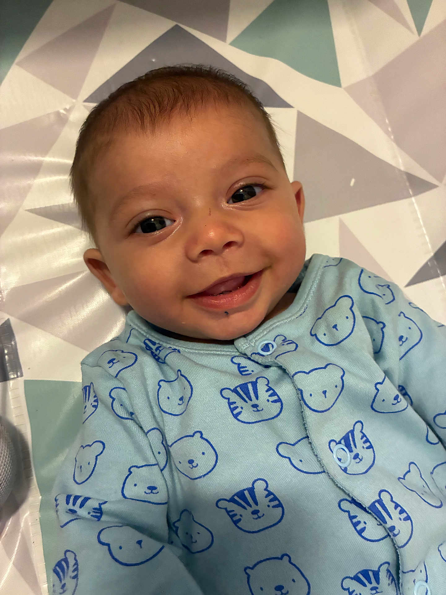 Anthony is registered to the contest to win money with this photo: baby, smile, face, infant, blue_onesie, bear_pattern, tiger_pattern, clothing, lying_down, geometric_pattern, mat, cute, happy, child, portrait, indoors, skin, head, eyes, mouth