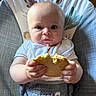 baby, infant, child, sitting, high_chair, cushion, bib, biscuit, cookie, food, snack, crumbs, eating, hands, face, eyes, smiling, portrait, indoor, blue_clothing