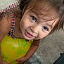 Kayleah is registered to the contest to win money with this photo: toddler, child, face, hair, eyes, dress, plaid, ball, yellow, carpet, hands, playing, indoor, person, cute, smile, skin, expression, young, curious
