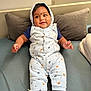 baby, child, smiling, hooded_onesie, animal_print, couch, cushion, footwear, sneakers, indoor, happy, person, infant, cute, relaxed, portrait, seated, cozy, casual, home