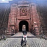 Nounours participe au concours pour gagner de l'argent avec cette photo : dog, border_collie, animal, pet, sitting, outdoor, historic_building, stone_archway, castle, fortress, gateway, cobblestone, architecture, travel, tourism, landmark, harness, black_and_white, portrait, sky