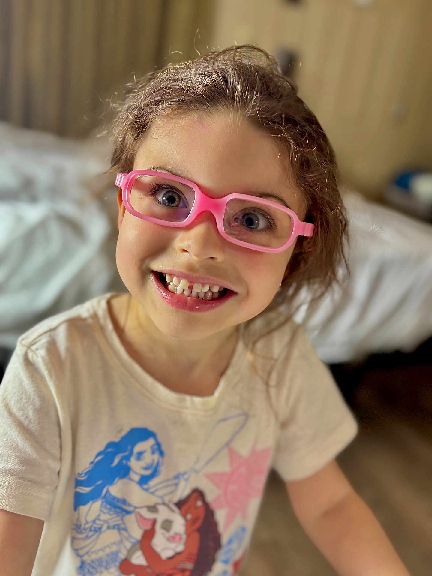 Mckenzie joined the competition — help win amazing prizes! child, girl, glasses, pink_glasses, smile, teeth, curly_hair, tshirt, indoor, bed, furniture, person, portrait, happy, young, cute, closeup, face, eyewear, casual