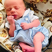 Jensen is registered to the contest to win money with this photo: newborn, baby, sleeping, infant, blanket, teddy_bear_pattern, pacifier, blue_clothing, romper, basket, soft_texture, cute, peaceful, tiny_feet, hand, portrait, indoors, cozy, child, resting