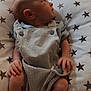 baby, infant, child, cushion, star_pattern, overalls, soft_toy, hand, foot, face, indoor, furniture, fabric, looking_sideways, cute, newborn, relaxing, resting, person, portrait
