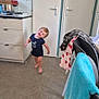 toddler, child, kitchen, floor, cabinet, door, towel, chair, smile, motion, barefoot, clothing, indoors, home, furniture, pot, stove, playful, happy, person