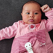 Laïane participe au concours pour gagner de l'argent avec cette photo : baby, infant, pink_clothing, lying_down, raised_fist, face, cheeks, pacifier_clip, curious_expression, child, cute, closeup, indoors, apparel, sleeves, soft_texture, human, skin, portrait, newborn