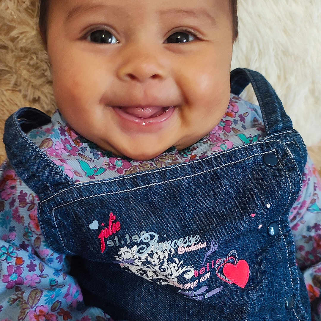 Laïane a rejoint le concours — aidez-le/la à gagner de superbes lots ! baby, child, closeup, clothing, cute, denim_overalls, eyes, face, floral_shirt, fluffy_background, hands, happy, indoor, infant, person, portrait, skin, smiling, soft_texture, tongue