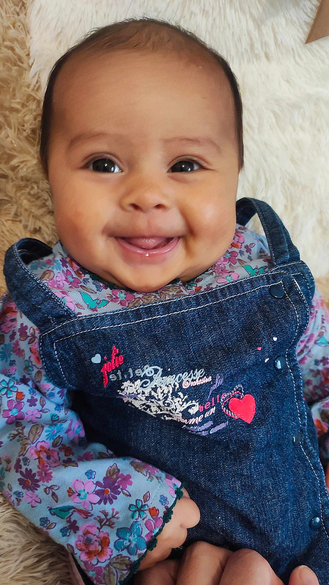 Laïane a rejoint le concours — aidez-le/la à gagner de superbes lots ! baby, smiling, denim_overalls, floral_shirt, cute, happy, infant, face, child, portrait, clothing, hands, person, indoor, soft_texture, fluffy_background, closeup, skin, eyes, tongue
