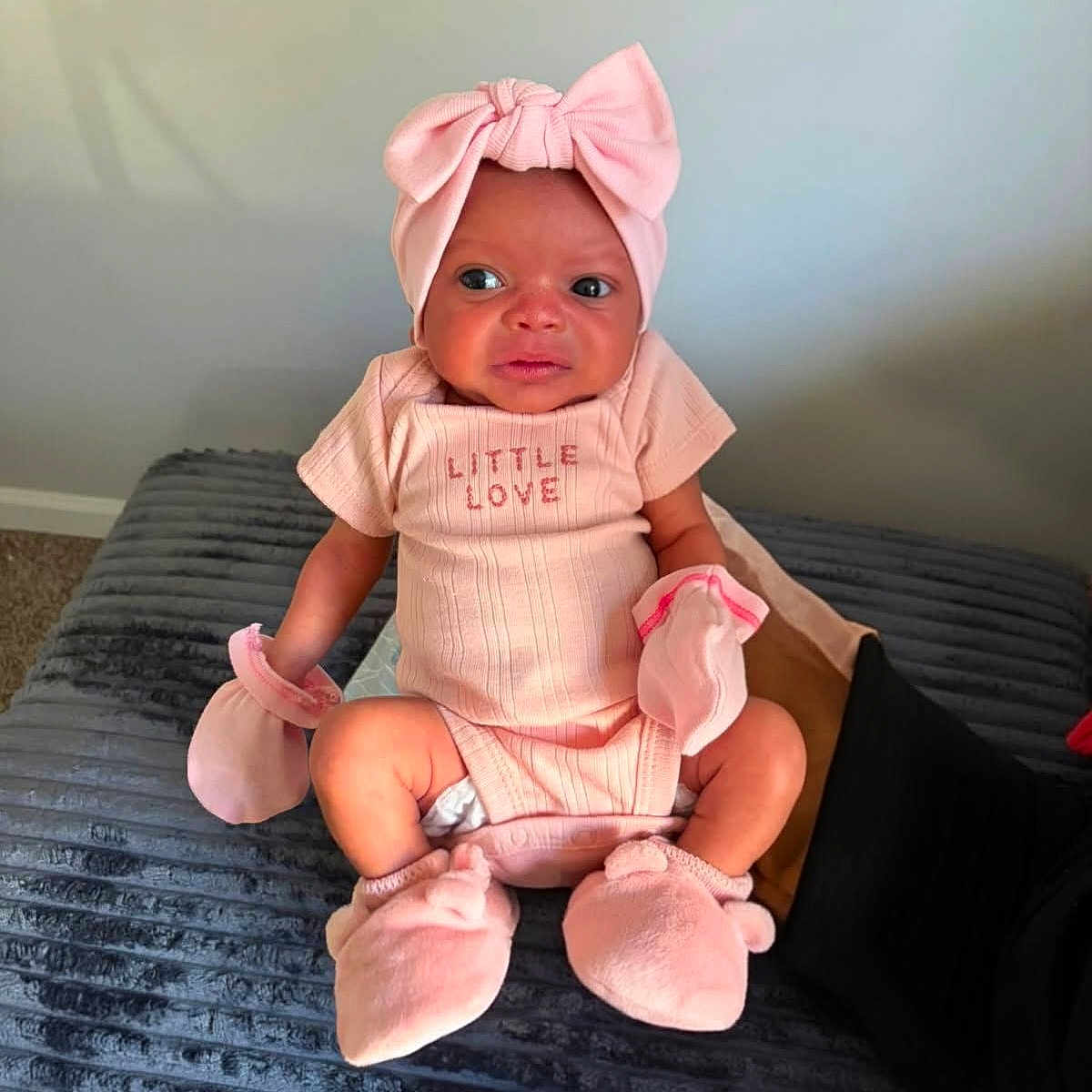 Kinsley is registered to the contest to win money with this photo: baby, infant, child, portrait, sitting, pink, bow, headband, onesie, mittens, booties, smiling, wide_eyed, bed, blanket, bedroom, indoor, fashion, cute, lifestyle
