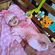 Nova Ann is registered to the contest to win money with this photo: baby, infant, pink, pajamas, hat, pom_pom, blanket, toy, wooden_crib, hand, smile, happy, indoor, person, child, colorful, pattern, holding_hand, cute, cozy