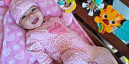Nova is registered to the contest to win money with this photo: baby, blanket, child, colorful_toys, cozy, cute, face, hand, happy, hat, holding_hand, indoor, infant, pajamas, patterned_clothing, pink_clothing, playtime, smiling, toy, wooden_crib