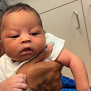 Racari Thompson joined the competition — help win amazing prizes! baby, infant, hand, tattoo, bracelet, smartwatch, diaper, white_clothing, skin, face, arm, fingers, cabinet, blue_blanket, indoor, person, holding, closeup, nursery, care