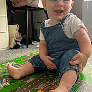 Joey joined the competition — help win amazing prizes! baby, carpet, child, clothing, colorful, daylight, denim_overalls, face, feet, furniture, happy, indoor, person, play_mat, room, sitting, smiling, toes, white_shirt, window