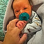 baby, infant, pacifier, hand, finger, blanket, dinosaur_pattern, pillow, cozy, sleepwear, newborn, cute, holding, closeup, skin, person, comfort, resting, indoors, soft