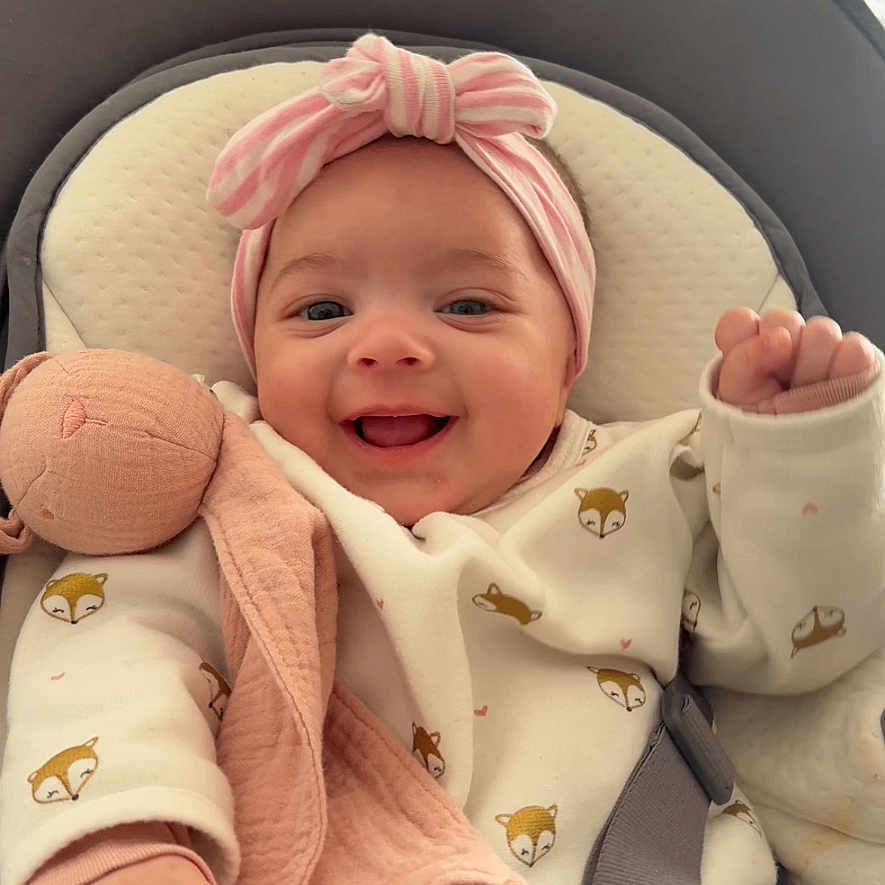 Alma a rejoint le concours — aidez-le/la à gagner de superbes lots ! baby, baby_seat, child, closeup, clothing, cute, face, happy, headband, indoors, infant, patterned_clothing, person, pink, plush_toy, seat_belt, smiling, soft_toy, toddler, white