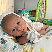 Silviano joined the competition — help win amazing prizes! baby, infant, pillow, animal_print, white_clothing, mittens, face, eyes, bedroom, toy, playmat, colorful, cute, resting, child, indoors, soft, comfort, head_support, gaze