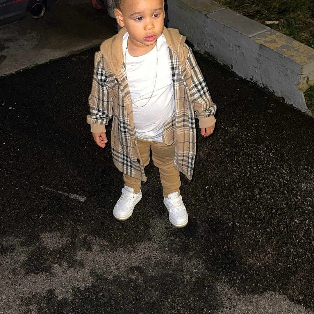 Ulysses joined the competition — help win amazing prizes! asphalt, casual_clothing, child, curious_expression, fashion, night, outdoor, pavement, person, plaid_jacket, side_view, standing, street, tan_pants, urban, wet_driveway, white_car, white_sneakers, yellow_building, young_child